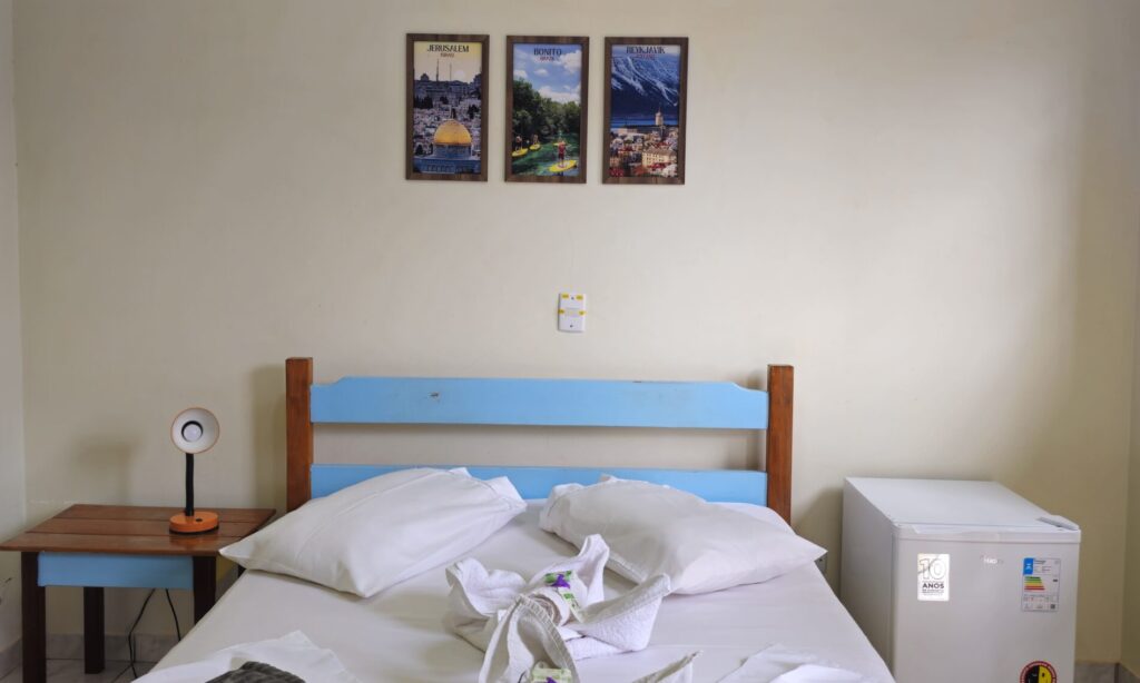 Suíte privativa, para duas pessoas. O quarto possui ar condicionado, frigobar e banheiro privativo. Está incluído no valor da hospedagem o café da manhã, uso da piscina e áreas comuns.